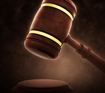 A wooden judge’s gavel held above a round sound block with a dark, softly lit background.