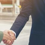Two people in business suits shaking hands outdoors, only their arms and torsos visible. - Ghassemi Law Group Two people in business suits shaking hands outdoors, only their arms and torsos visible