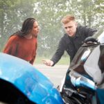 A woman and a man stand beside two damaged cars on a road, appearing to discuss the aftermath of a car accident. - Ghassemi Law Group A woman and a man stand beside two damaged cars on a road, appearing to discuss the aftermath of a car accident