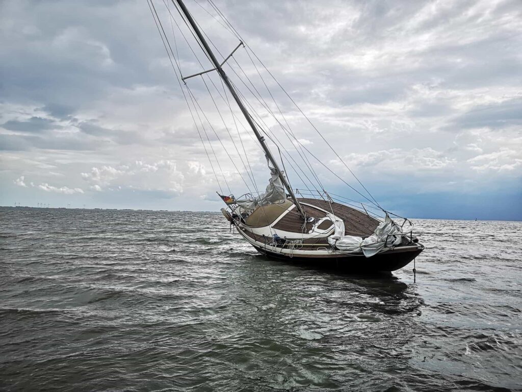 A sailboat is tilted heavily to one side in choppy water under a cloudy sky, illustrating the risks of boating accidents.