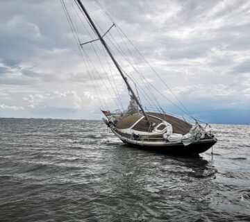 A sailboat is tilted heavily to one side in choppy water under a cloudy sky, illustrating the risks of boating accidents.