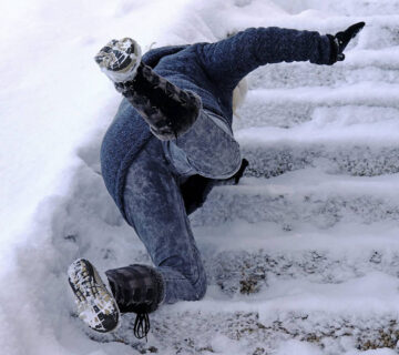 A person experiences a slip and falls on snowy outdoor steps, dressed in winter clothing and boots.