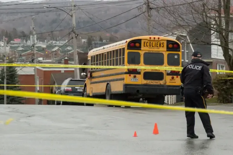 A police officer stands near traffic cones and yellow tape blocking a street where a school bus is parked, with buildings and hills in the background. - Ghassemi Law Group - Ghassemi Law Group A police officer stands near traffic cones and yellow tape blocking a street where a school bus is parked, with buildings and hills in the background