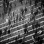 Black and white photo of a crowded crosswalk with blurred figures of people walking in different directions, evoking the chaotic potential for a pedestrian accident