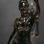 A bronze statue of Lady Justice holding scales and a sword, wearing a blindfold, stands against a blurred background—a symbol often invoked in wrongful death cases