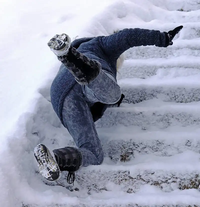 Person slipping and falling on snow covered outdoor steps, wearing winter clothes and boots, surrounded by snow 