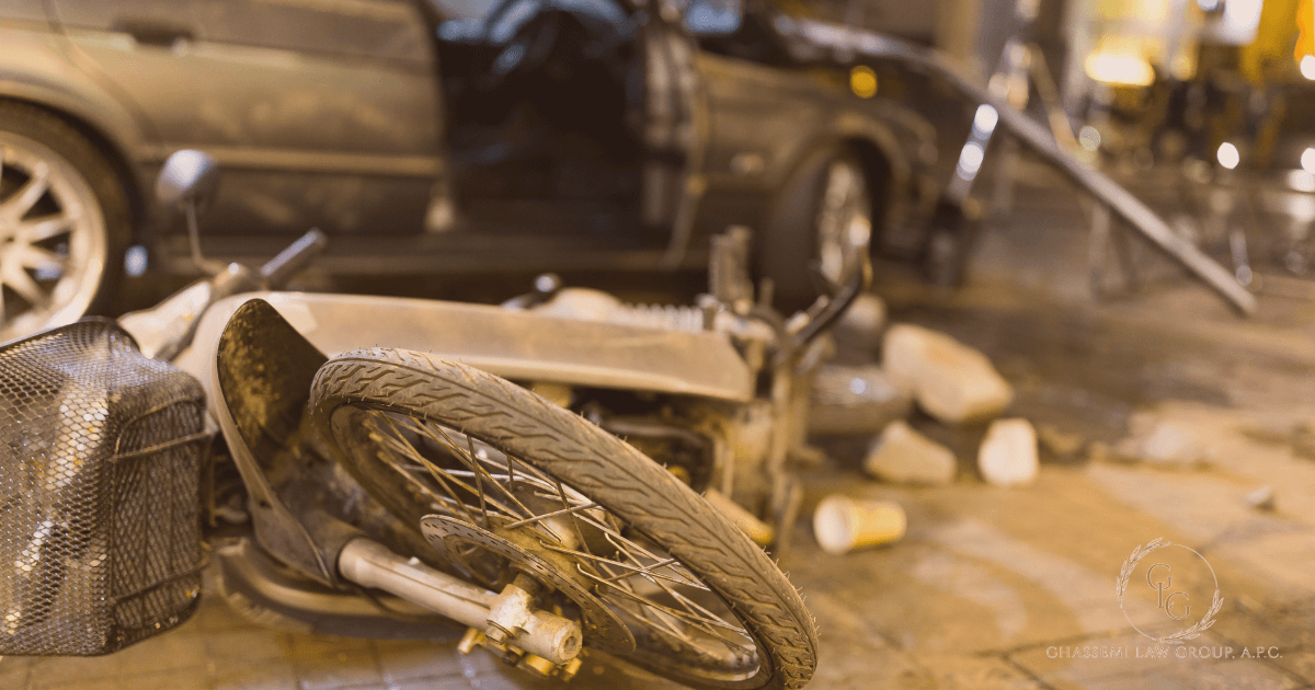 A damaged motorcycle lies on its side near scattered debris and a car with an open door, suggesting a recent accident on a city street.