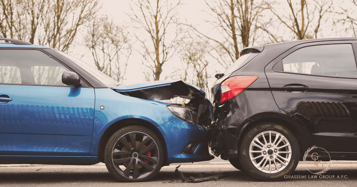 A blue car has rear ended a black car on a road, resulting in visible damage to both vehicles. Trees are in the background.