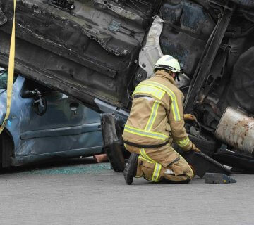 A firefighter in protective gear kneels beside an overturned vehicle stacked on a crushed car during a rescue operation—reminding us how vital expert help, like a Car Accident Lawyer in Irvine, can be when you need it most. - Ghassemi Law Group A firefighter in protective gear kneels beside an overturned vehicle stacked on a crushed car during a rescue operation—reminding us how vital expert help, like a Car Accident Lawyer in Irvine, can be when you need it most.