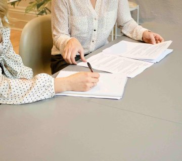 Two people in polka dot shirts sit at a table reviewing and writing on documents with a personal injury lawyer in Irvine. - Ghassemi Law Group Two people in polka dot shirts sit at a table reviewing and writing on documents with a personal injury lawyer in Irvine.