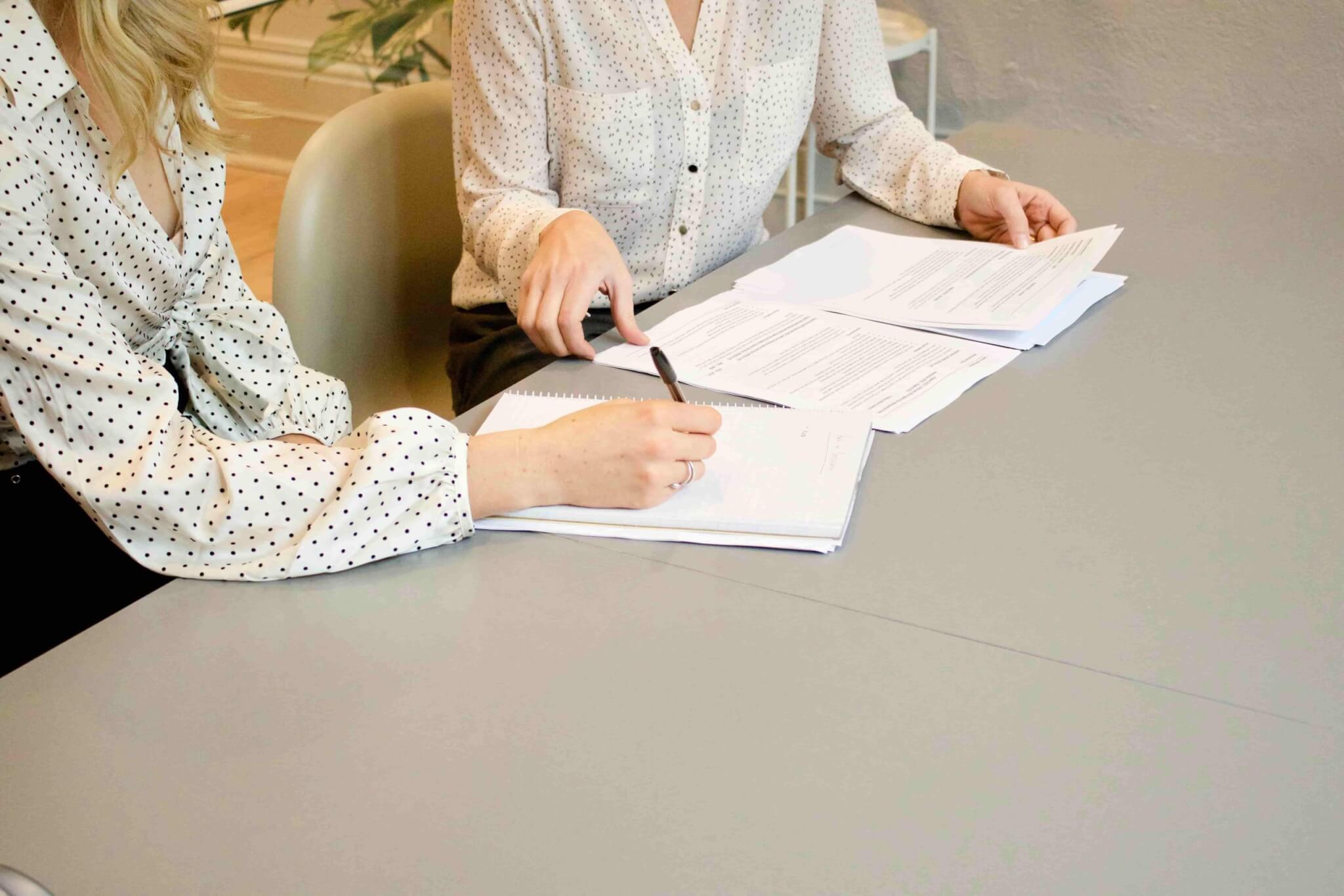 Two people in polka dot shirts sit at a table reviewing and writing on documents with a personal injury lawyer in Irvine. - Ghassemi Law Group Two people in polka dot shirts sit at a table reviewing and writing on documents with a personal injury lawyer in Irvine.