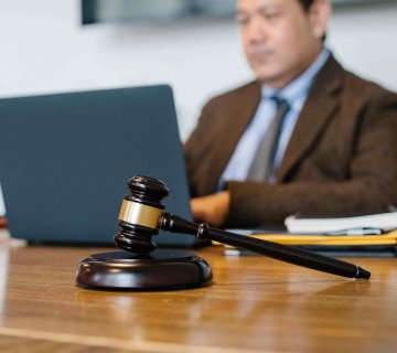 A wooden gavel rests on a desk in the foreground, while a lawyer for a minor car accident works on a laptop in the blurred background. - Ghassemi Law Group A wooden gavel rests on a desk in the foreground, while a lawyer for a minor car accident works on a laptop in the blurred background.