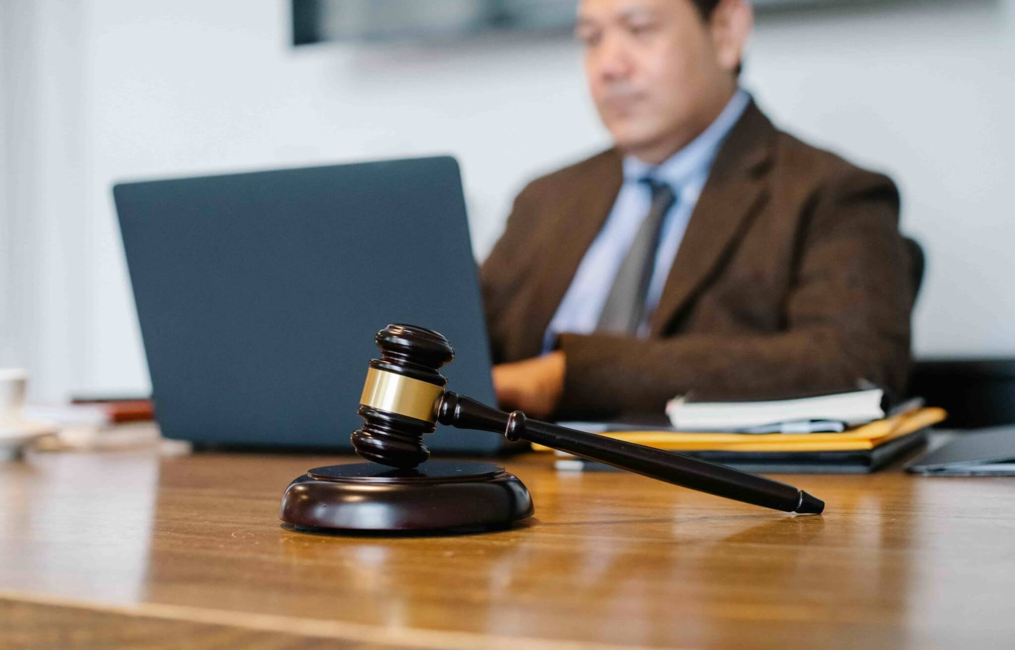 A wooden gavel rests on a desk in the foreground, while a lawyer for a minor car accident works on a laptop in the blurred background. - Ghassemi Law Group A wooden gavel rests on a desk in the foreground, while a lawyer for a minor car accident works on a laptop in the blurred background.