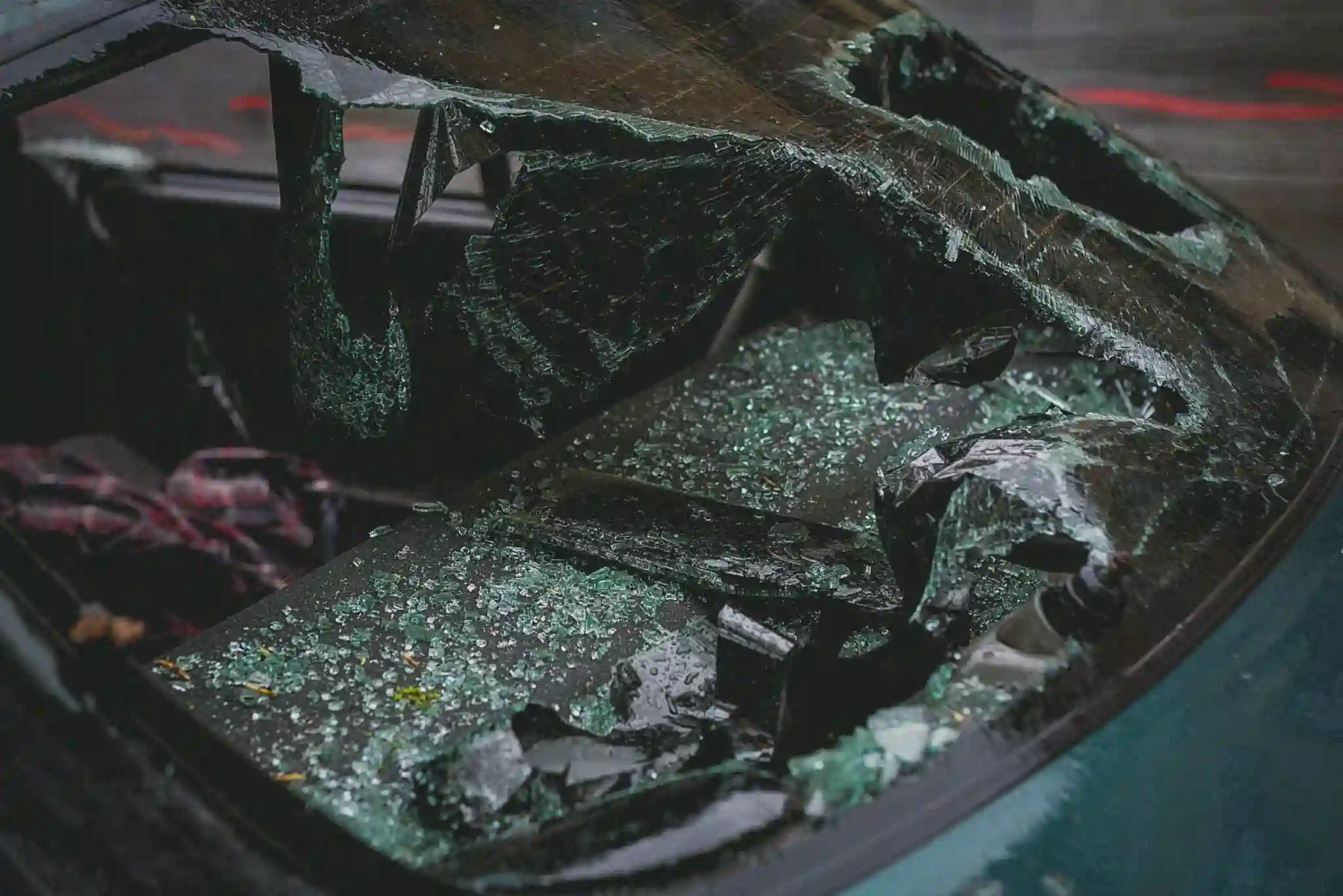 A car windshield is severely shattered, with large broken glass pieces scattered on the car’s hood and interior, suggesting the possibility of a burn injury amid the chaotic aftermath. - Ghassemi Law Group A car windshield is severely shattered, with large broken glass pieces scattered on the car’s hood and interior, suggesting the possibility of a burn injury amid the chaotic aftermath