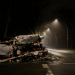 A heavily damaged car is wrapped in caution tape at night beside an empty, dimly lit road. - Ghassemi Law Group A heavily damaged car is wrapped in caution tape at night beside an empty, dimly lit road