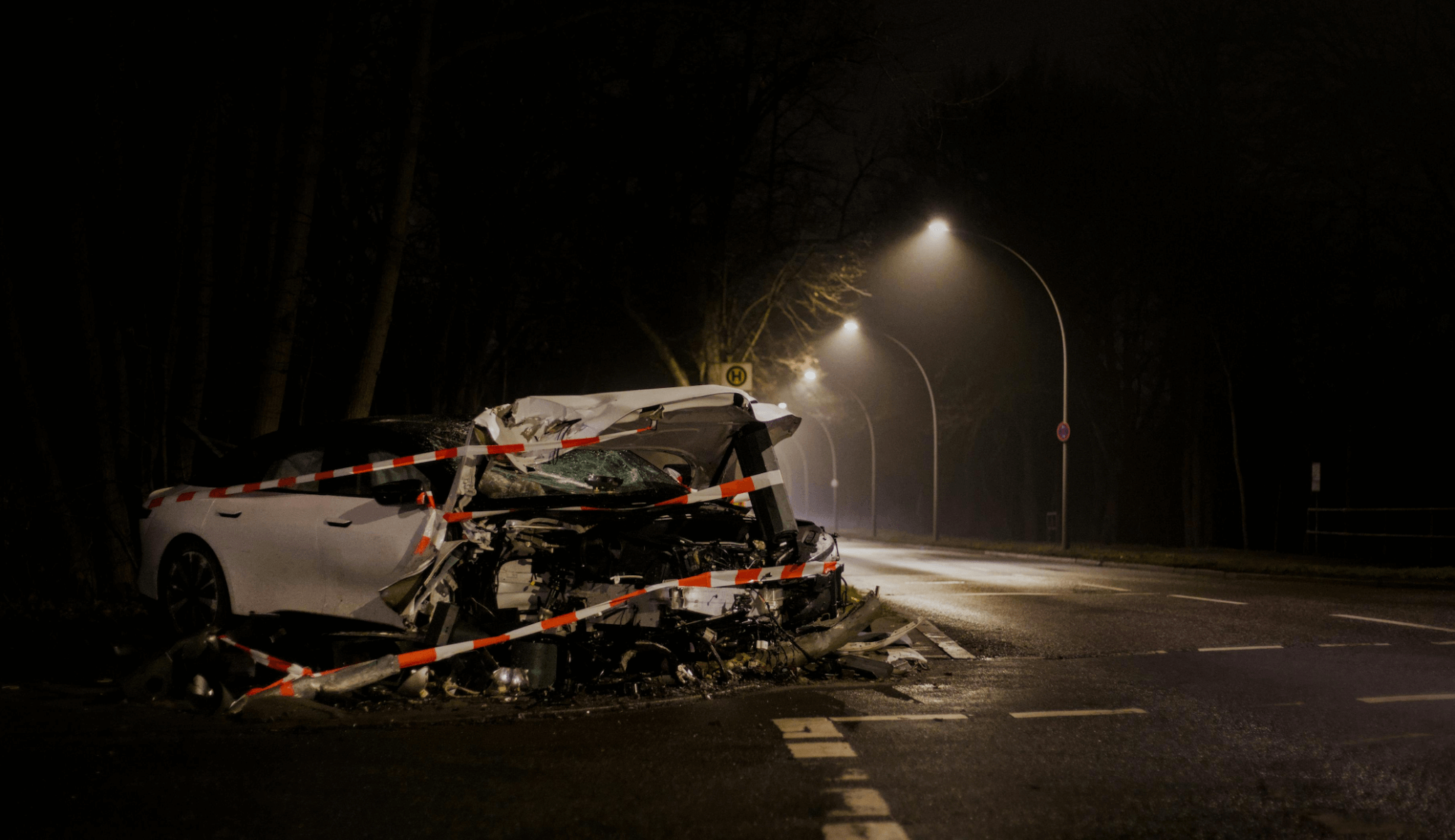 A heavily damaged car is wrapped in caution tape at night beside an empty, dimly lit road. - Ghassemi Law Group A heavily damaged car is wrapped in caution tape at night beside an empty, dimly lit road