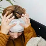 A person wearing a mustard sweater sits holding their head, which is bandaged with gauze, appearing distressed. - Ghassemi Law Group A person wearing a mustard sweater sits holding their head, which is bandaged with gauze, appearing distressed