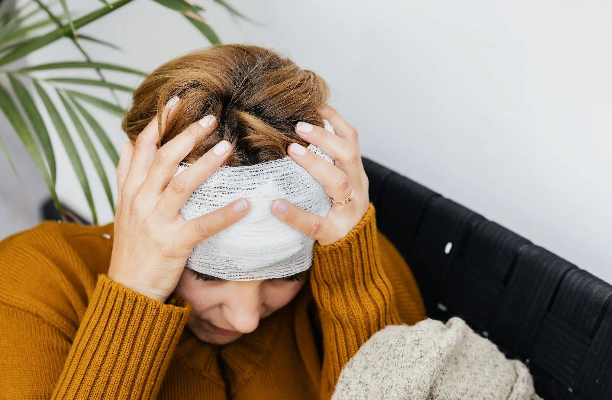 - Ghassemi Law Group A person wearing a mustard sweater sits holding their head, which is bandaged with gauze, appearing distressed