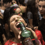 At a crowded party with colored lights, a woman holds a green bottle near her mouth, appearing to drink—an image reminding us that Drunk Driving Accidents in Irvine: Seeking Maximum Compensation is crucial for those affected. - Ghassemi Law Group At a crowded party with colored lights, a woman holds a green bottle near her mouth, appearing to drink—an image reminding us that Drunk Driving Accidents in Irvine: Seeking Maximum Compensation is crucial for those affected