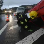A firefighter examines an overturned red car after an accident on a wet road, with cones and another damaged vehicle nearby—raising the question: What Should I Do Immediately After a Car Accident in Irvine?. - Ghassemi Law Group A firefighter examines an overturned red car after an accident on a wet road, with cones and another damaged vehicle nearby—raising the question: What Should I Do Immediately After a Car Accident in Irvine?