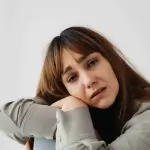 A woman with brown hair leans on her knees, looking distressed or upset, against a plain white background, depicting the emotional turmoil often experienced after an accident. Can I Sue for Emotional Distress After an Accident in Irvine?. - Ghassemi Law Group A woman with brown hair leans on her knees, looking distressed or upset, against a plain white background, depicting the emotional turmoil often experienced after an accident Can I Sue for Emotional Distress After an Accident in Irvine?