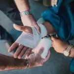 A person wraps gauze bandage around another person's injured hand while both are seated, raising the question: How Long Do I Have to File a Personal Injury Claim in Irvine?. - Ghassemi Law Group A person wraps gauze bandage around another person's injured hand while both are seated, raising the question: How Long Do I Have to File a Personal Injury Claim in Irvine?
