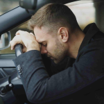 A man sits in the driver’s seat of a car, resting his forehead on the steering wheel with his eyes closed, appearing stressed or exhausted—perhaps wondering, "How long will it take to settle my car accident case in Irvine?. - Ghassemi Law Group A man sits in the driver’s seat of a car, resting his forehead on the steering wheel with his eyes closed, appearing stressed or exhausted—perhaps wondering, "How long will it take to settle my car accident case in Irvine?