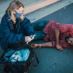 A person wearing a mask and gloves prepares medical supplies next to a man lying on his side on the pavement near a curb, raising questions such as, "How long do I have to file a pedestrian accident claim in California?. - Ghassemi Law Group A person wearing a mask and gloves prepares medical supplies next to a man lying on his side on the pavement near a curb, raising questions such as, "How long do I have to file a pedestrian accident claim in California?