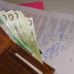 A brown wallet filled with Polish banknotes is placed on top of a handwritten document with blue ink, resembling files you might see when researching What Is the Average Settlement for a Car Accident Injury in Irvine. - Ghassemi Law Group A brown wallet filled with Polish banknotes is placed on top of a handwritten document with blue ink, resembling files you might see when researching What Is the Average Settlement for a Car Accident Injury in Irvine
