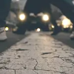 Close up of a cracked street line with two people crossing, their legs in motion, and blurred car headlights in the background