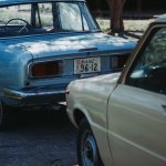 Two vintage cars, one blue and one beige, are parked closely together on a shaded outdoor surface—a potential scene for discussing how do I prove negligence in a car accident case in Irvine The blue car’s rear and license plate are visible