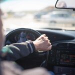 Person driving a car, holding the steering wheel with one hand  The dashboard and part of the road outside the windshield are visible, capturing a moment that could easily be examined in a Drunk Driving case 