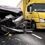 A severely damaged silver car is shown after a truck accident involving a yellow truck on a highway Debris and glass cover the road