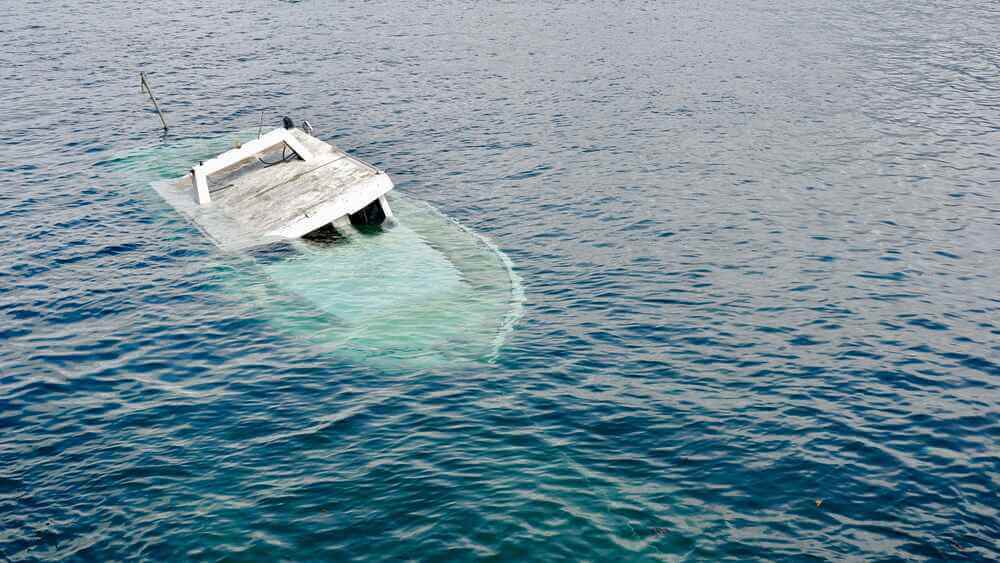 A partially submerged white boat is sinking in calm blue water, with only part of the cabin and hull visible above the surface. - Ghassemi Law Group A partially submerged white boat is sinking in calm blue water, with only part of the cabin and hull visible above the surface