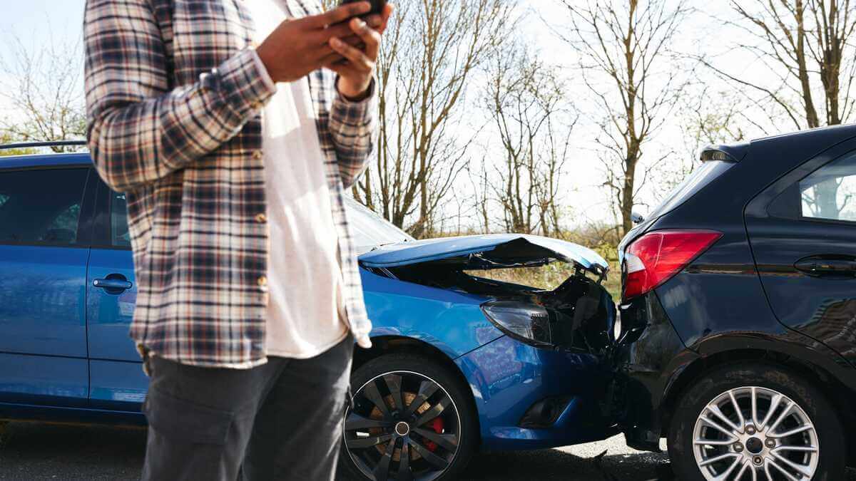 A person using a smartphone stands near two cars involved in a rear end collision on a road 