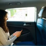 Woman sitting in the back seat of a car using her phone, while a man drives in the front seat. - Ghassemi Law Group Woman sitting in the back seat of a car using her phone, while a man drives in the front seat