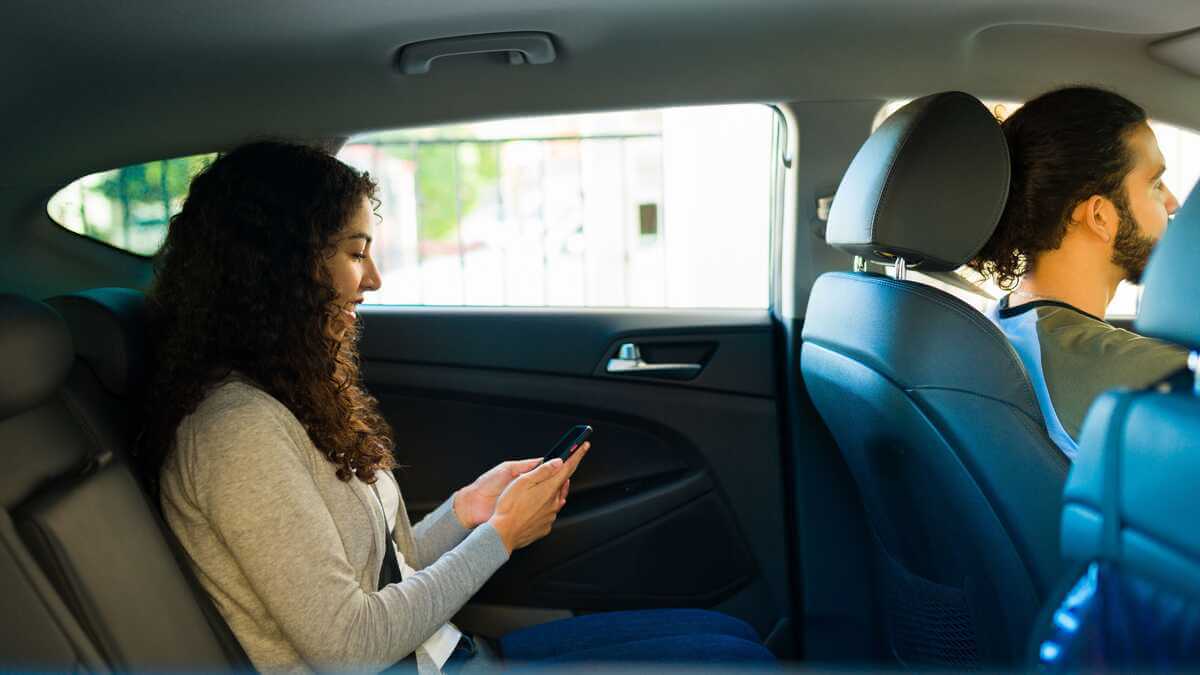 Woman sitting in the back seat of a car using her phone, while a man drives in the front seat 